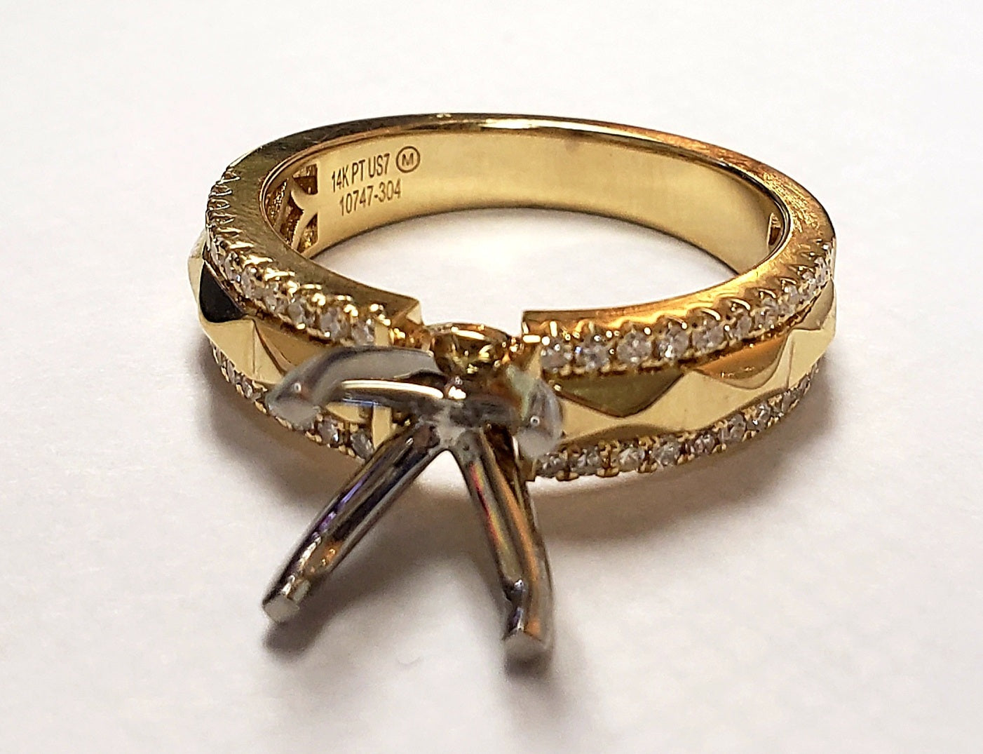 Gold ring with a prong-setting for a diamond, surrounded by a row of smaller diamonds. 