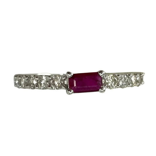 Ring with a central ruby stone and diamond-studded band on a white background