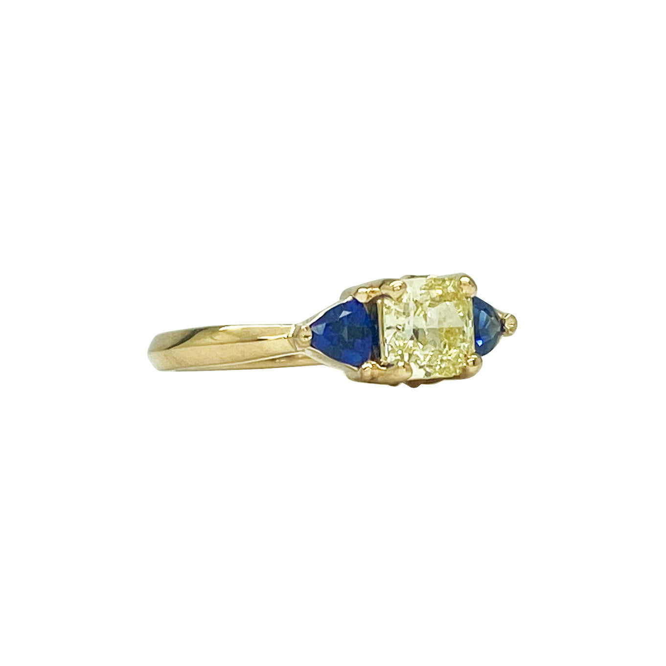 Gold ring with a yellow diamond in the center, flanked by two blue sapphires. The ring is set in a classic three-stone setting. Side view