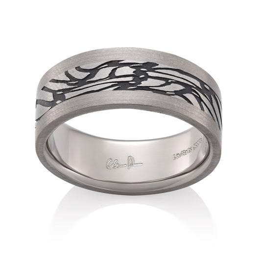 Silver ring with a textured, patterned center on a white background.