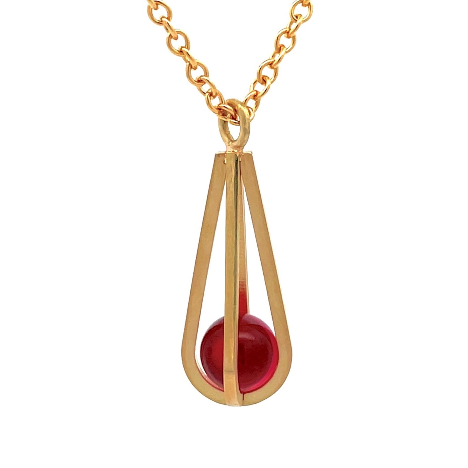 Gold pendant shaped like a teardrop, with a red gemstone suspended inside, on a white background