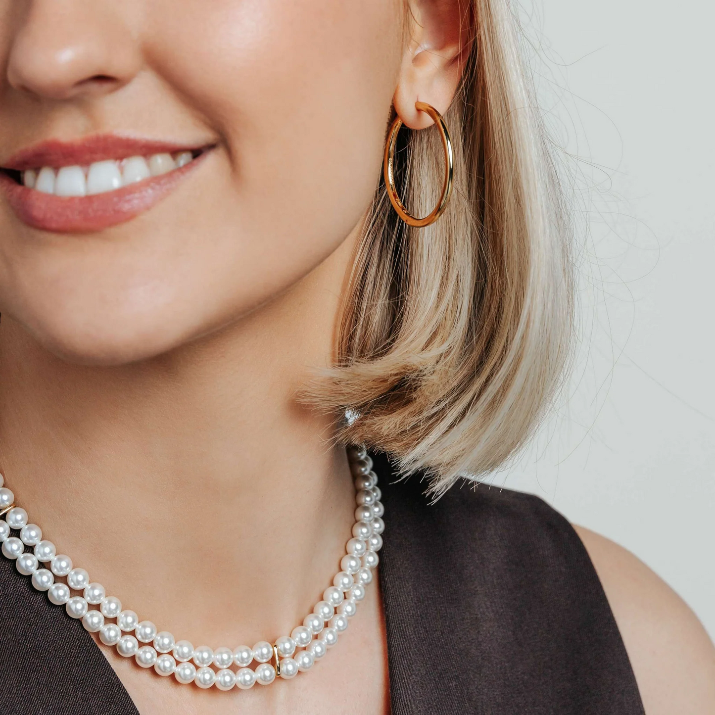 Close-up of a woman wearing gold hoop earrings and pearl necklaces.