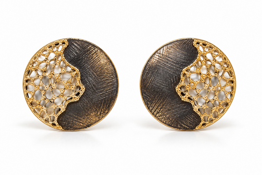 A pair of round gold and dark metal earrings with a split design featuring textured brushed metal and an openwork filigree pattern, shown on a white background.