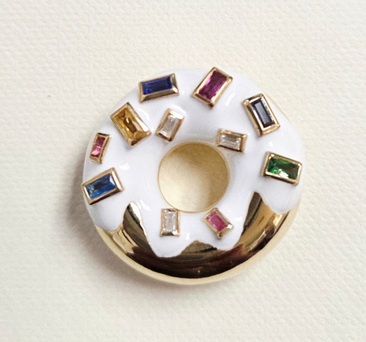 white gold donut-shaped pendant with gold and gemstone embellishments on a beige background