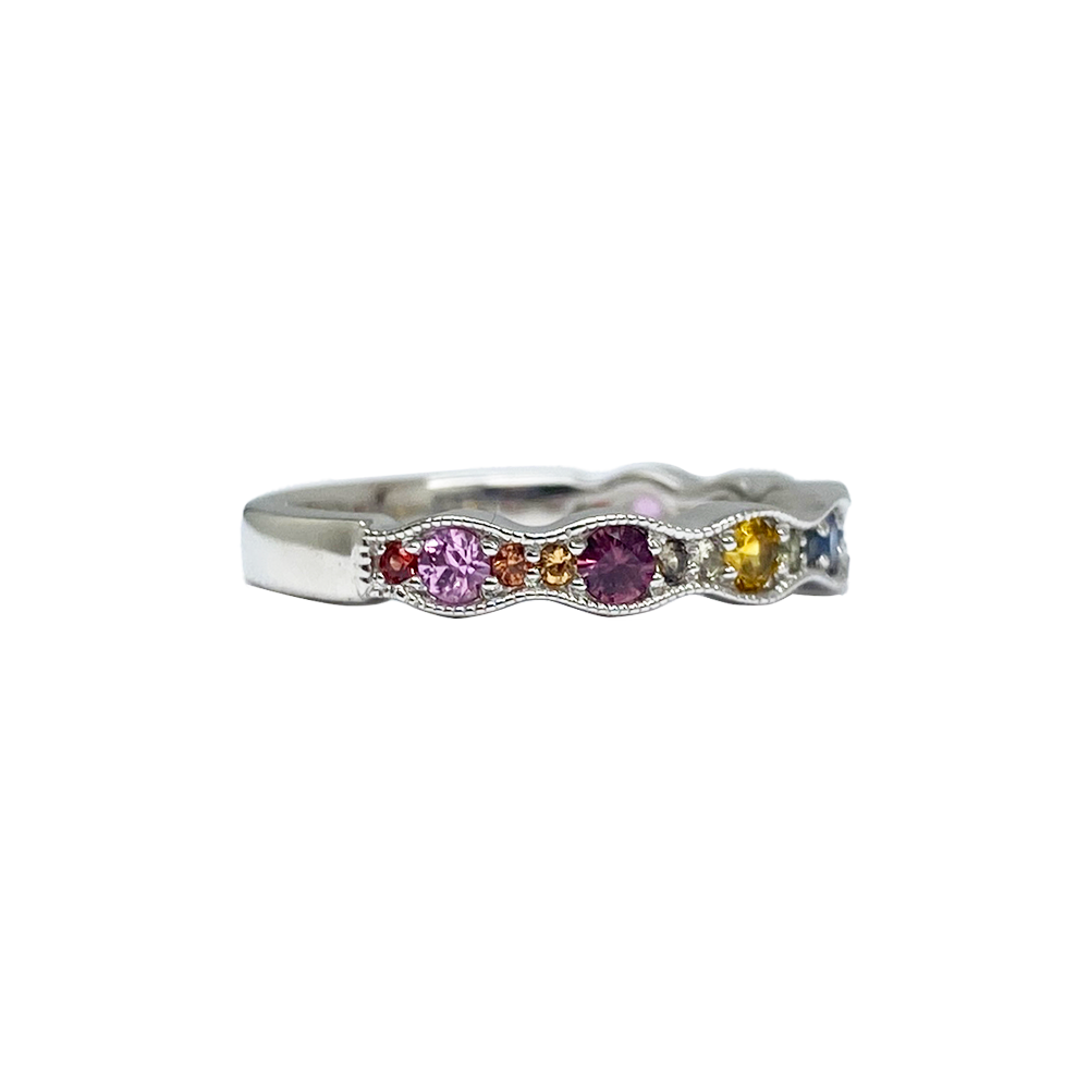 Side view of silver multi-gemstone ring with a wavy band featuring round sapphires in various colors including pink, purple, blue, yellow, and orange. 